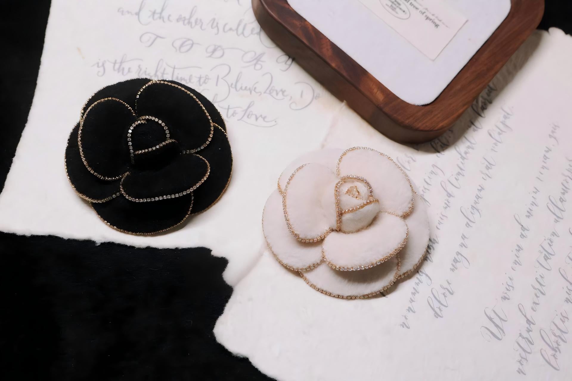 Camellia brooches in black and pearl white with gold beaded accents on fabric