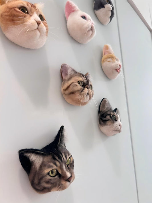 Multiple cat-paw felt fridge magnets arranged on a light wall