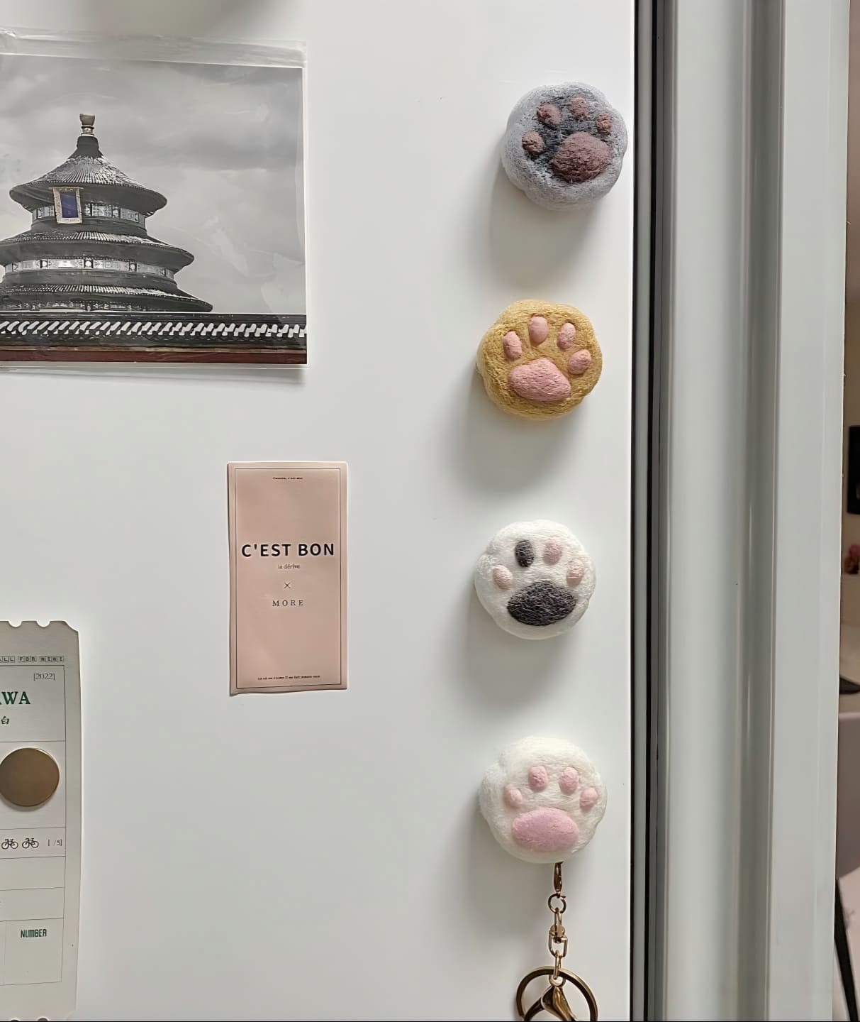 Four cat face fridge magnets on a white door, with a tan paw-print and key chain