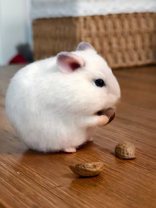 Plush white hamster in side view, dark eyes and pink nose, near small nuts
