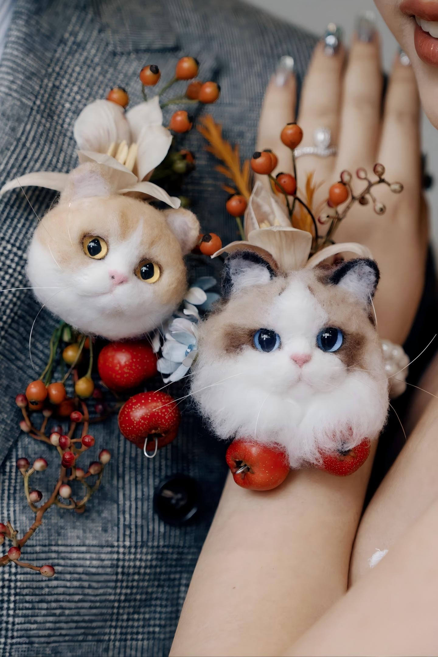 Pet souvenir cat plush pair with berry and seed decorations on a person's hand