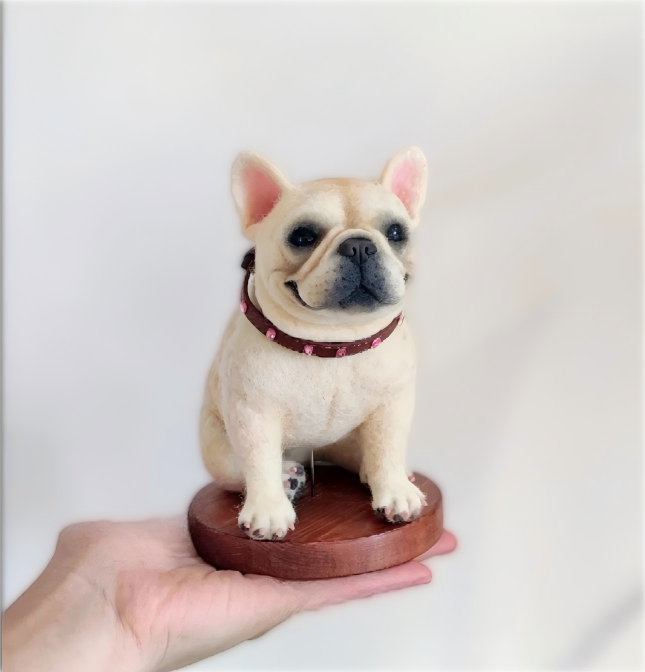 French bulldog figurine with red collar on round wooden base, held in hand