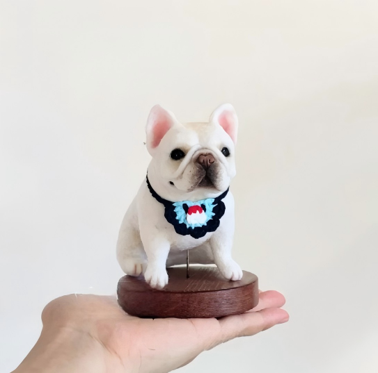 French bulldog figurine with blue red bow tie on round wooden base in hand