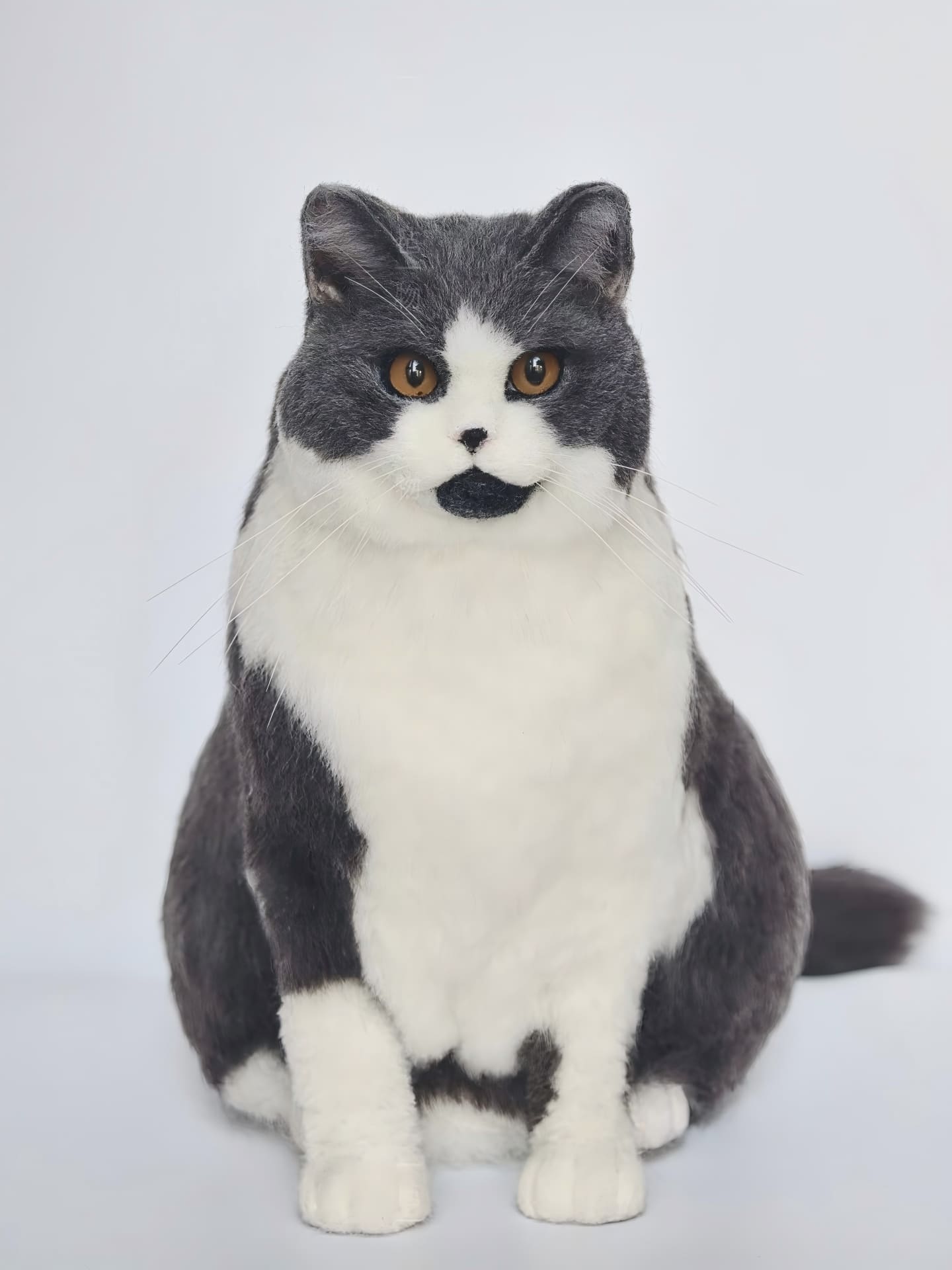 Cat figurine with black and white fur, sitting front view and amber eyes